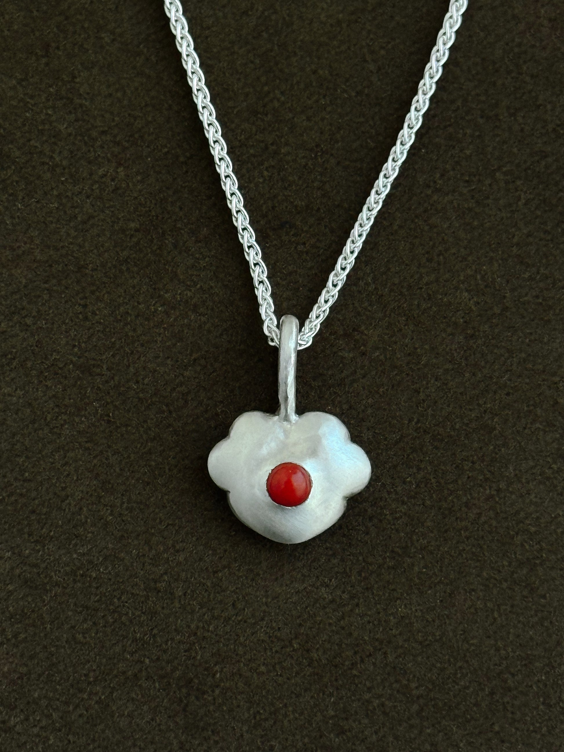 Silver necklace with a five-petal heart-shaped pendant featuring a coral stone on a dark background